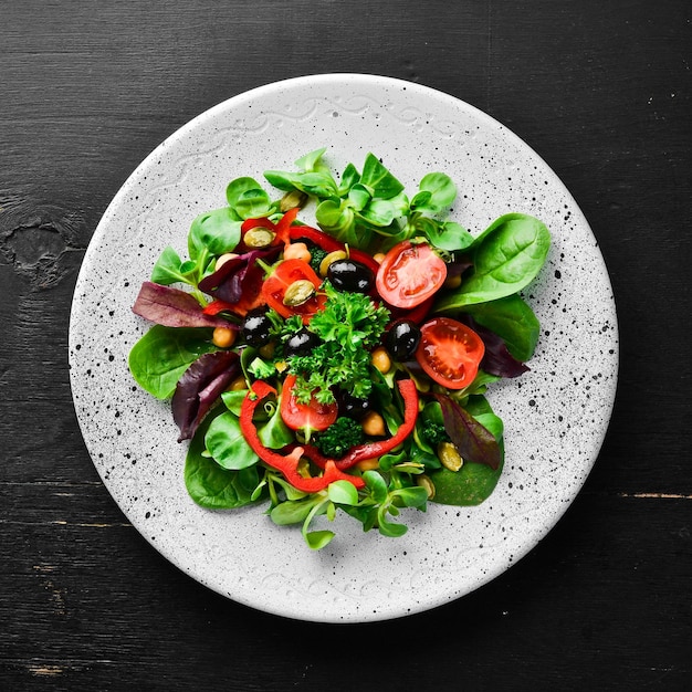 Vegetable salad with spinach tomatoes paprika and pumpkin seeds in a plate on a wooden background Top view Free space for your text Flat lay