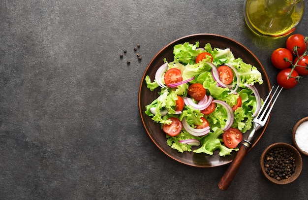 Vegetable salad with tomatoes, red onions and sauce on black, top view