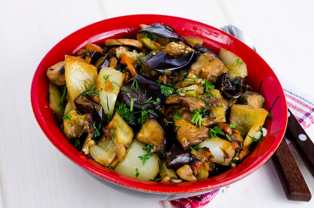 Vegetable saute with eggplants in ceramic bowl on white wooden table