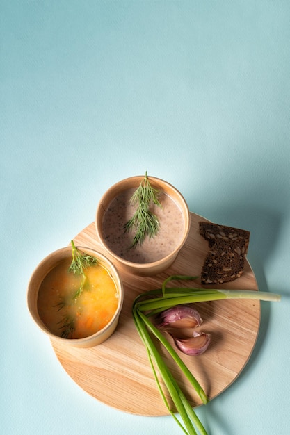 Фото Овощный суп и грибковый кремовый суп в бумажных одноразовых чашках для доставки или доставки продуктов питания