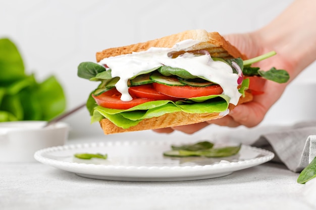 Vegetable vegan sandwich with white sauce tomato spinach cucumber Woman hand taking toast