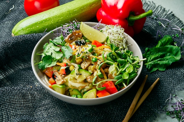 Vegetable vegan wok in a gray bowl on a gray cloth in a composition with vegetables. Delicious vegetarian food. Diet Menu.