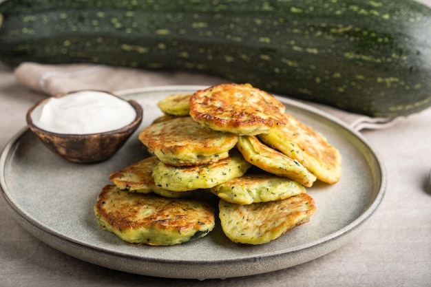 Vegetable vegetarian zucchini pancakes with sour cream on a round plate and green zucchini