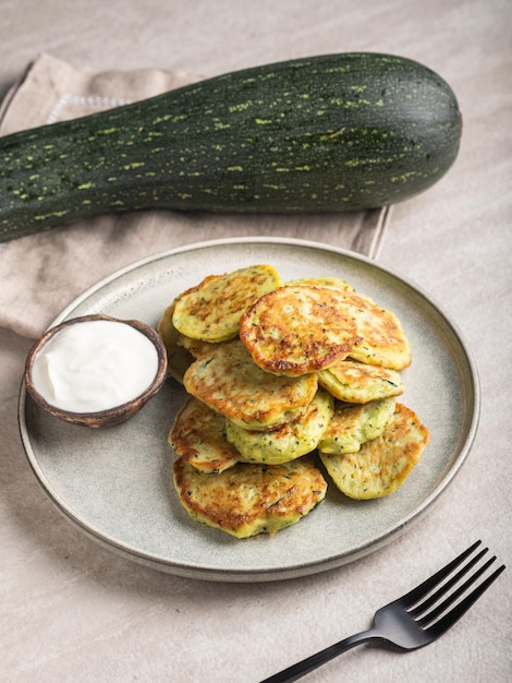 Vegetable vegetarian zucchini pancakes with sour cream on a round plate and green zucchini