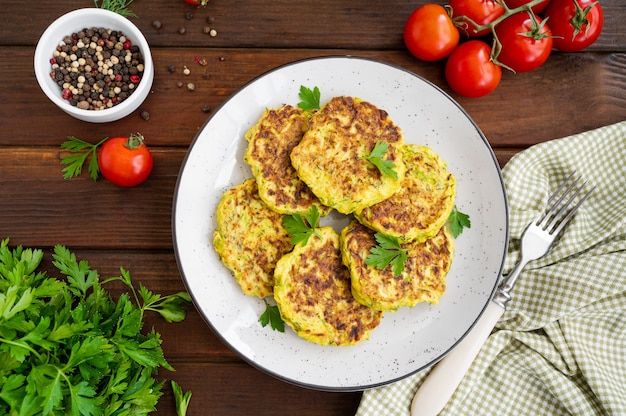 Vegetable zucchini pancakes with cheese, dill and parsley on a plate with sour cream