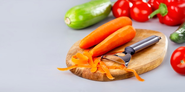 Vegetables banner. Vegetables cooking and eating. Peeling raw carrot and different vegetables at wooden board.