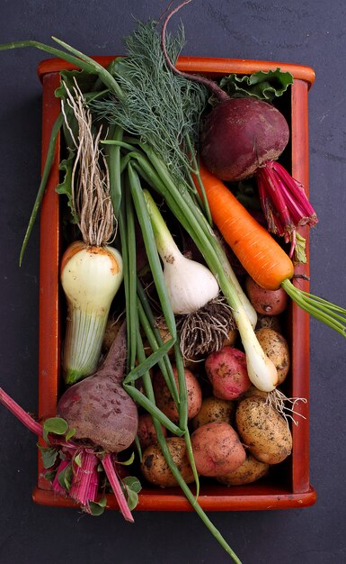 Vegetables in a basket: beets, onions, garlic, dill, potatoes, carrots on an old wooden background