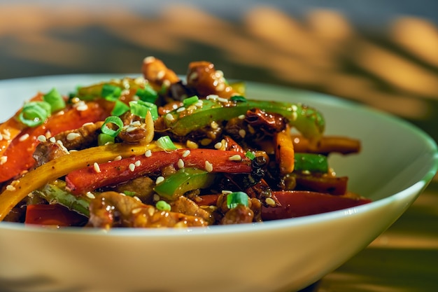 Photo vegetables and beef in sweet and sour sauce with sychang pepper. wood background. chinese cuisine