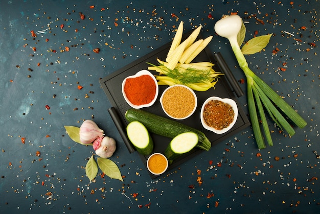 THE VEGETABLES IN THE BOX ON THE STONE A DARK. YOUNG GREENS ONION GARLIC ZUCCHINI BRIGHT SPICES LAY IN A WOODEN TRAY WITH HANDLES ON A DARK TEXTURED.