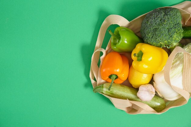 Vegetables in eco fabric bag on green surface top view zero waste lifestyle concept