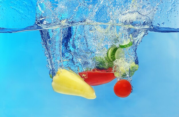 Vegetables falling into water on color background