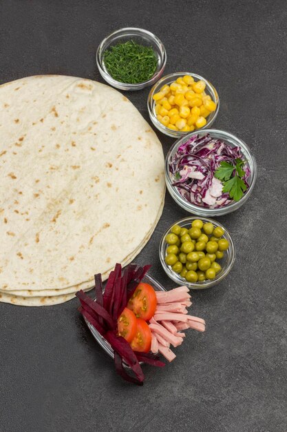 Riempimento di verdure per la tortilla in ciotole di vetro tortilla avvolte sfondo nero pianeggiante