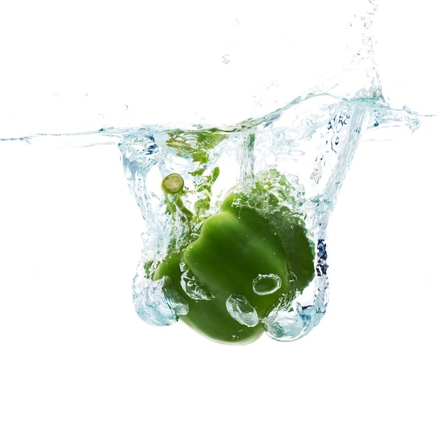 Photo vegetables, food and healthy eating concept - close up of fresh green pepper falling or dipping in water with splash over white background