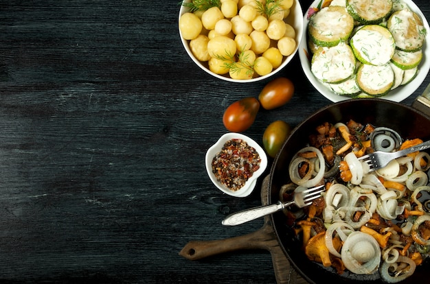 Vegetables . Fried zucchini sauce in a plate. Young boiled potatoes with dill in a bowl. Fried chanterelle mushrooms with golden onions in a frying pan. copyspace