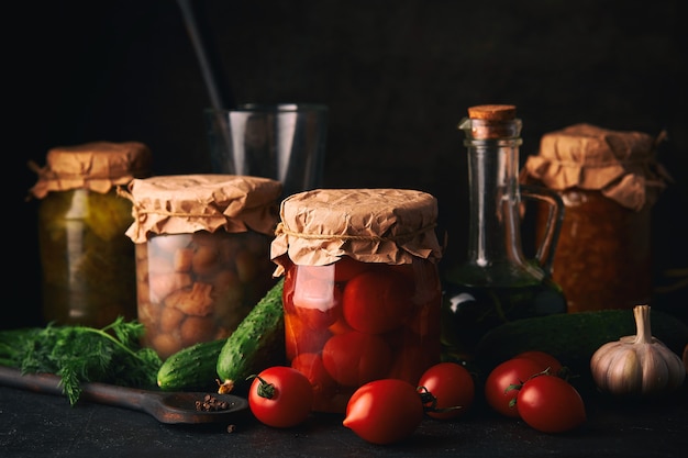 Vegetables and fruits canning. Glass jars with fermented, pickled and canned vegetables and fruits on dark rustic kitchen table.