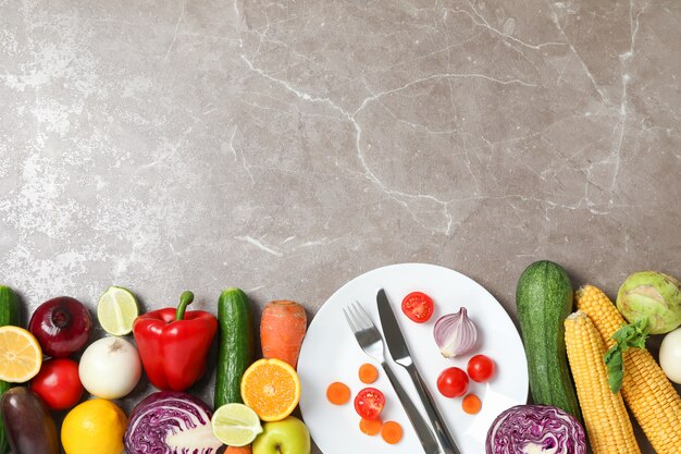 Vegetables, fruits, plate and cutlery on grey 