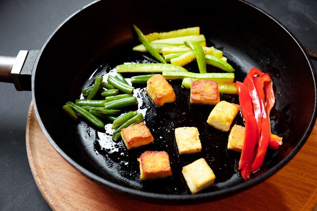Vegetables in a frying pan are fried. Black background.