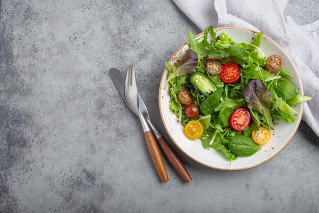 Vegetables healthy salad with red and yellow cherry tomatoes pepper and green salad leafs on white rustic ceramic plate