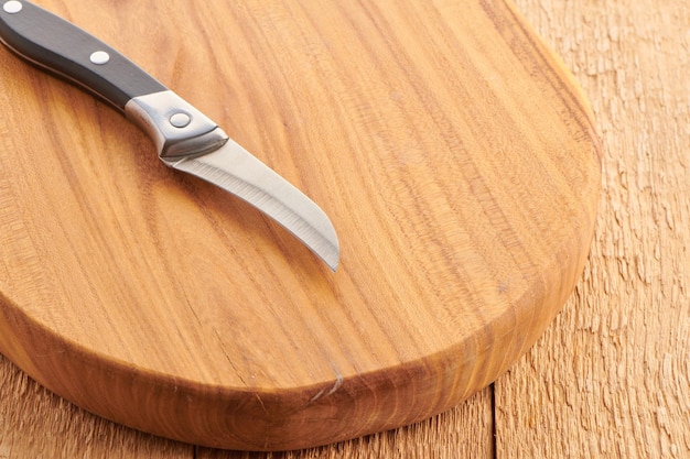 Vegetables knife with curved blade on empty round wooden cut board Knife for cooking closeup view Kitchen equipment