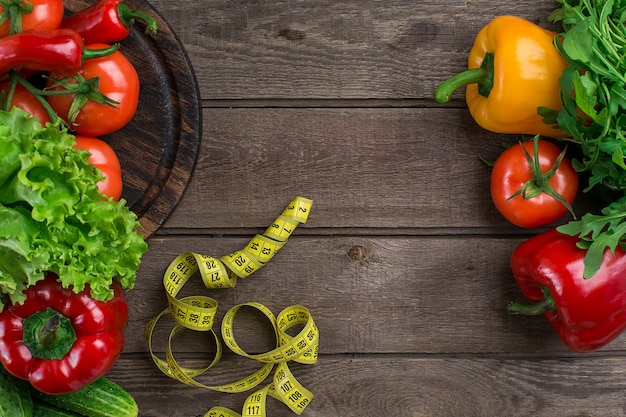 Vegetables and in measure tape in diet on wooden background. Top view. Copy space