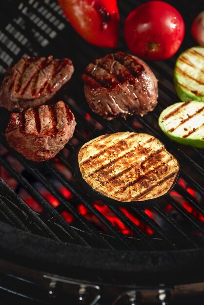 Vegetables and meat sizzling on the grill with flames, close up