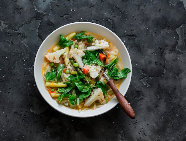 Vegetables and orzo pasta vegetarian minestrone soup on a dark background top view