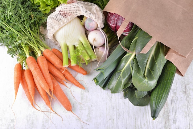 Verdure in un sacchetto di carta tra altre verdure fresche su un tavolo bianco