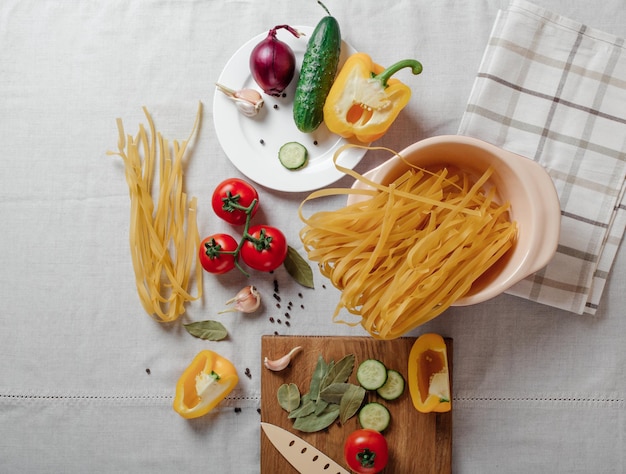 Vegetables and raw pasta on a table Cherry tomatoes yellow bell pepper cucumber red onion and garlic