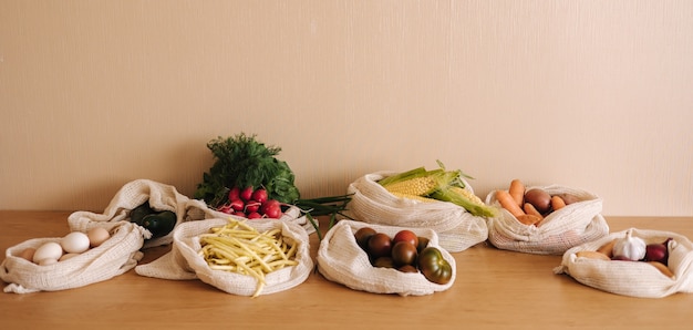 Vegetables in reusable eco cotton bags on wooden table. Zero waste shopping concept. Canvas grocery bag with tomatoes, carrot, potato. Plastic free items