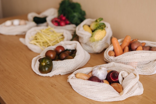 Vegetables in reusable eco cotton bags on wooden table. Zero waste shopping concept. Canvas grocery bag with tomatoes, carrot, potato. Plastic free items