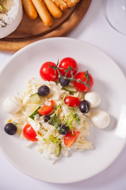 Insalata di verdure sul piatto e piatto con formaggi assortiti, frutta e altri spuntini.