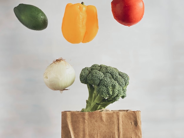 Vegetables tomato, bell pepper, onion, broccoli levitating over a paper bag for shopping. Healthy lifestyle and nutrition concept.