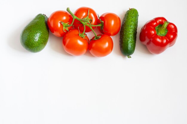 Vegetables on white, avocado, tomatoes on a branch, cucumber and sweet pepper