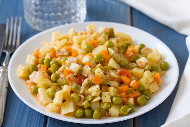 Verdure con il pesce sul piatto e sul bicchiere d'acqua bianchi