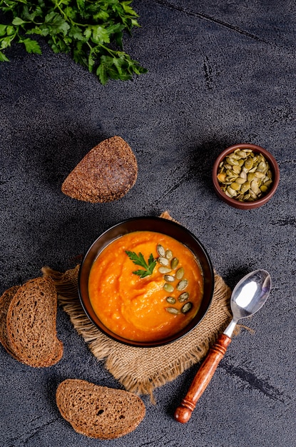 Vegetarian autumn cream soup of pumpkins and carrots with seeds and parsley on a dark table