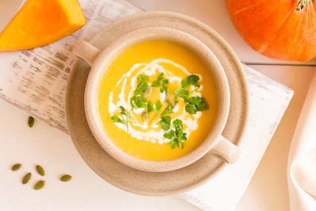 Vegetarian autumn pumpkin cream soup with pumpkin seeds served in a bowl with sour cream and parsley. top view.