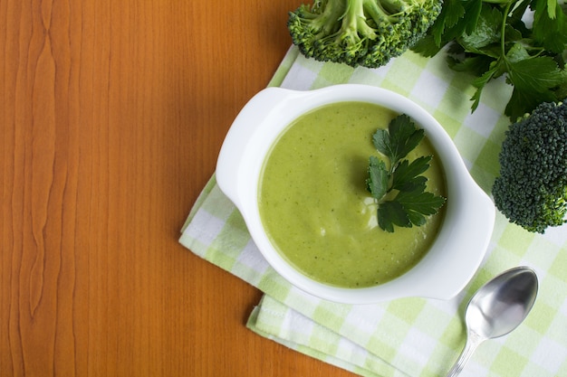 Vegetarian broccoli puree soup in the white bowl on the light brown wooden