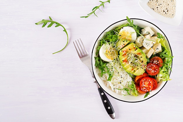 vegetarian buddha bowl lunch with eggs, rice, tomato, avocado and blue cheese on table. 