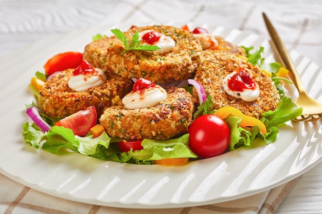 Vegetarian burgers, patties of legume, onion and greens served on a white plate with fresh salad and tomato sauce, horizontal view from above