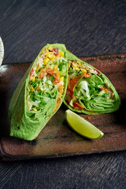 Vegetarian burrito with rice, tomatoes, corn and bell pepper in green pita on a brown plate with tomato salsa and guacamole. Vegetarian Shawarma Roll