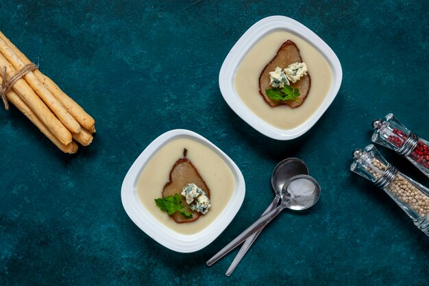 Vegetarian celery root homemade cream-soup with blue cheese, fresh caramelized pear and breadsticks