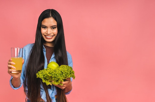 Vegetarian concept Healthy happy asian woman holding a bowl of fresh lettuce green apple and orange juice isolated over pink background Healthy lifestyle