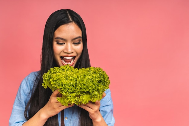 Vegetarian concept Healthy happy asian woman holding a bowl of fresh lettuce isolated over pink background