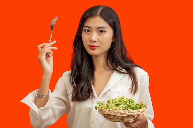 Vegetarian concept Healthy woman eating sunflower sprouts standing isolated over orange background