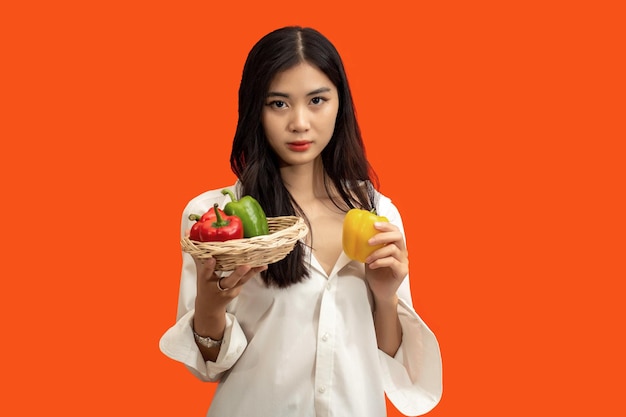 채식주의 개념 건강한 여성은 주황색 배경에 격리된 다채로운 피망 바구니를 들고 있습니다.