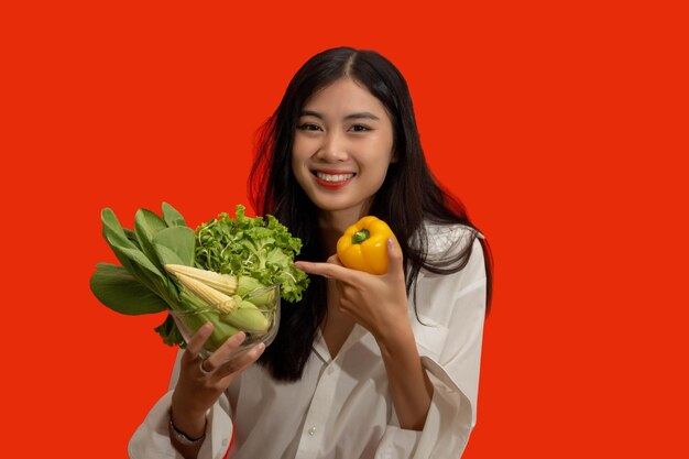 Vegetarian concept Healthy woman hold bell pepper and bowl of fresh vegetable on orange background