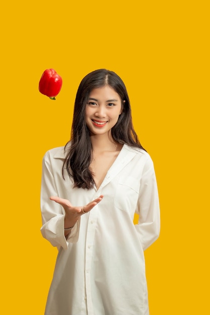 Vegetarian concept Healthy woman is throwing up colorful bell pepper on isolated yellow background