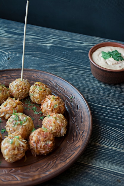 Vegetarian croquettes of potatoes and cabbage with sauce, vegetables and herbs. Packed in parchment. Tasty and satisfying. Dark wooden background. Side view.