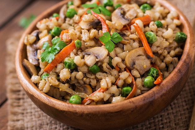 Vegetarian crumbly pearl barley porridge with mushrooms and green peas in a wooden bowl