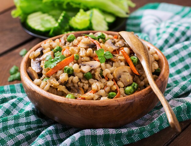 Vegetarian crumbly pearl barley porridge with mushrooms and green peas in a wooden bowl